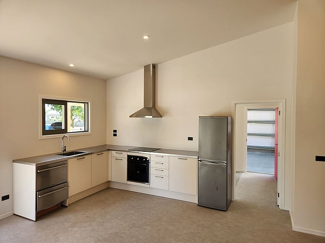 The kitchen with cream cabinetry and a stainless benchtop, looking through to the garage