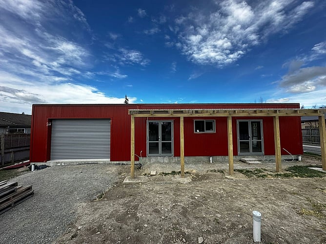 Front of the red shed home: roller door, two sets of French doors and the timber pergola