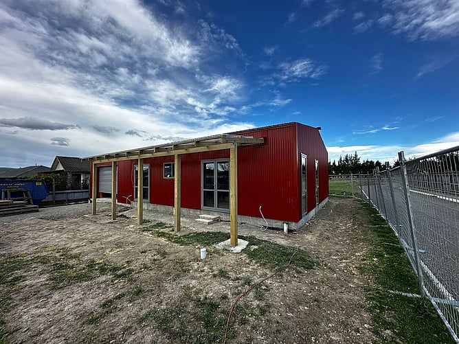 Side view of the red shed home with the verandah pergola framed up, before landscaping