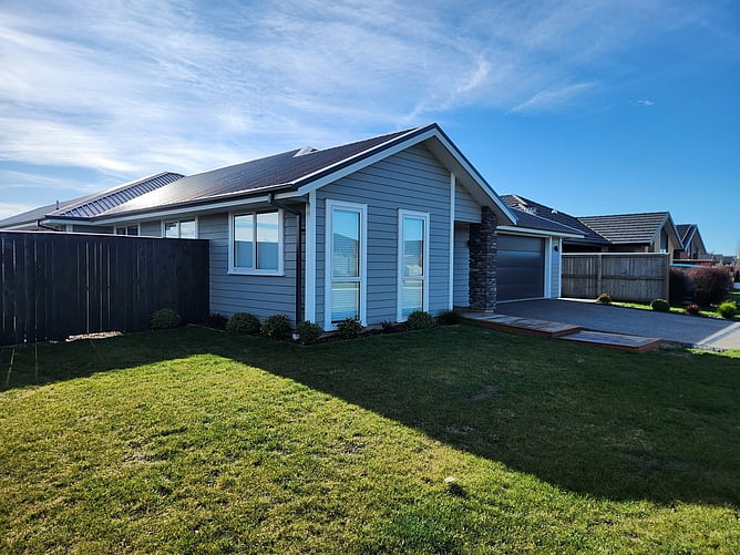 The street side of the Rolleston showhome: Linear cladding, white joinery, a schist column beside the garage and timber deck steps