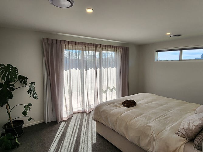 A bedroom in the Rolleston showhome, with sheer curtains over the slider and a high window for extra light