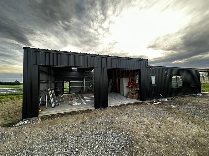 The Lincoln shed home mid-build, black cladding on, with the two tall garage door openings and the living-area door still open