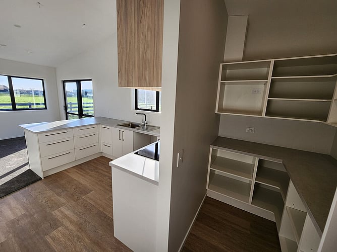 The kitchen and the added pantry: white cabinetry, timber overhead cupboards and open shelving, with the paddocks through the window