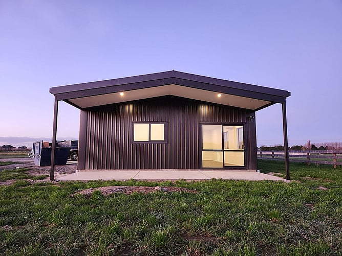 The covered patio at dusk, with the lights on inside the Lincoln shed home