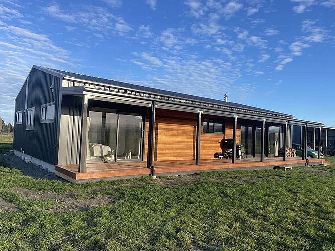 The finished Kaikoura home: dark steel cladding, a horizontal cedar feature wall and Kwila decking along the living side, under a big blue sky