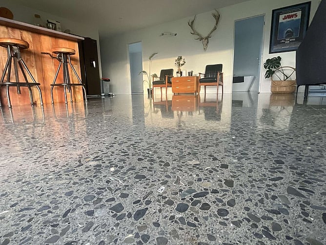 Close-up of the polished concrete floor, with paua shell inlaid among the stone and the kitchen stools behind