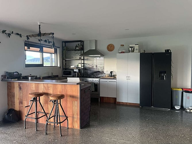 The kitchen, with its timber-clad island and bar stools on the polished concrete floor, and the hills through the window