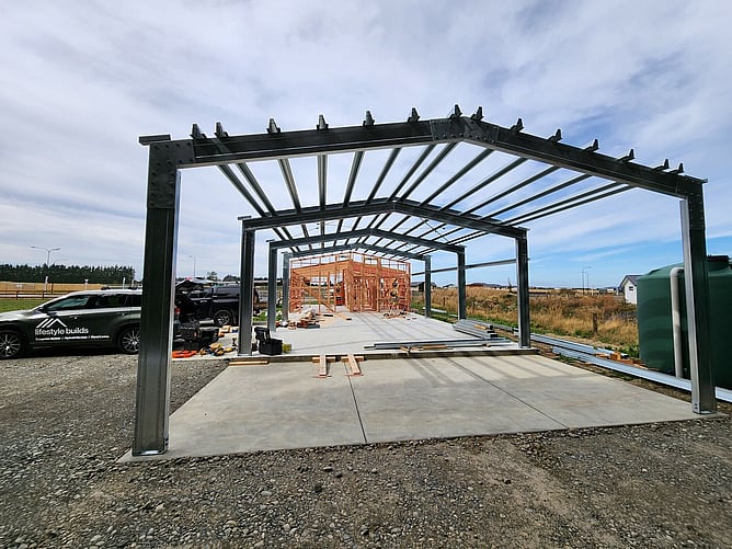 Looking through the steel garage and carport bays to the timber framing, with a Lifestyle Builds vehicle parked on site