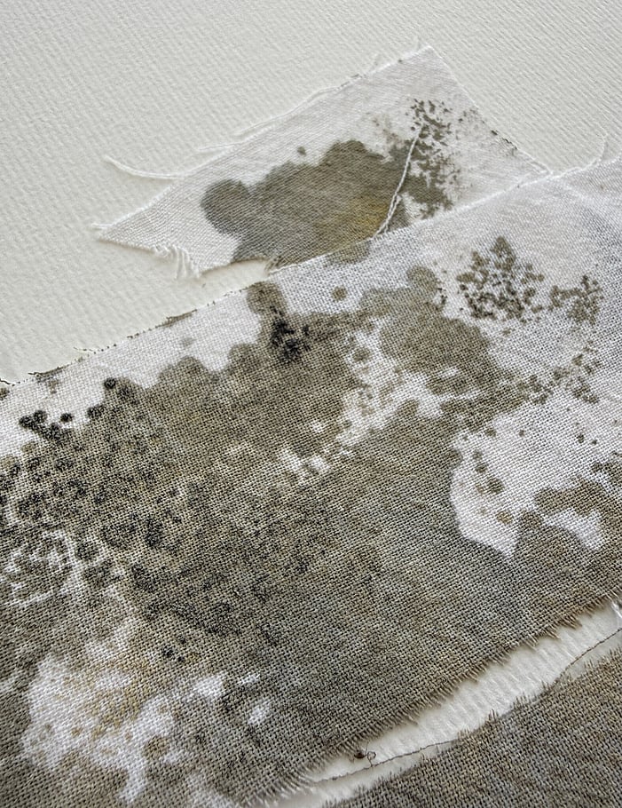 first detail image of layered repurposed pale cream cotton fragments blotted with green-grey, raw sienna and black acrylic, showing visible weave texture and soft frayed edges 