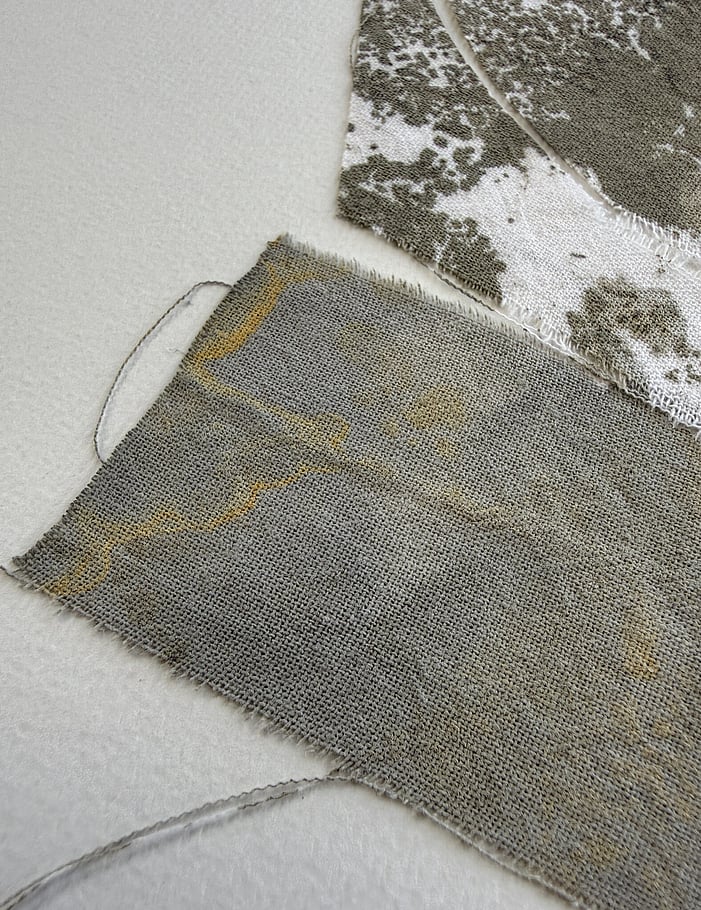 second detail image of layered repurposed pale cream cotton fragments blotted with green-grey and raw sienna  acrylic, showing visible weave texture and soft frayed edges 