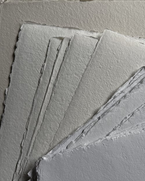 image of several overlapping sheets of handmade paper in neutral tones, showing their varied textures and natural edges
