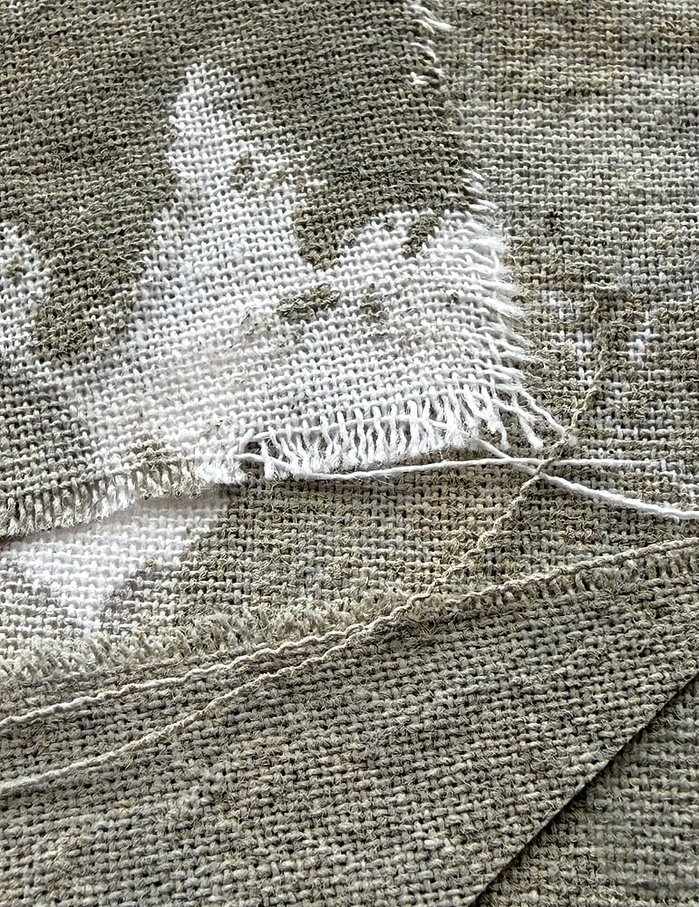 close-up image of pale oat-toned cotton fragments hand-painted with green-grey acrylic, showing visible weave texture and soft frayed edges