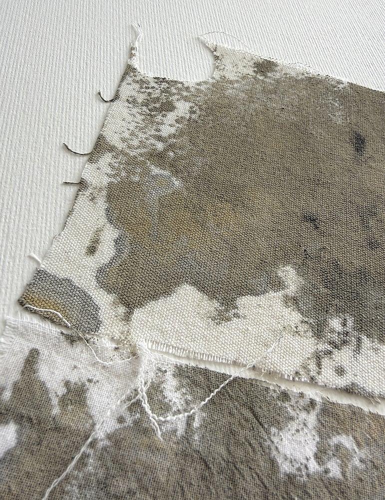 close-up image of layered repurposed oat-toned cream cotton fragments hand-painted with green-grey, black and raw sienna  acrylic, showing visible weave texture and soft frayed edges 