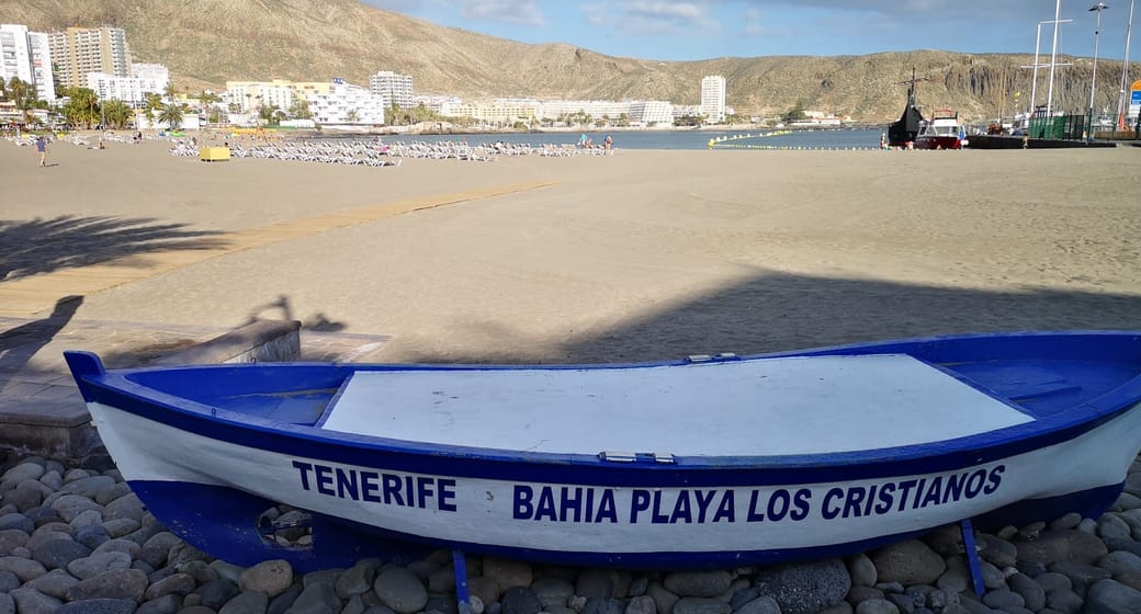 Playa de Los Cristianos beach with a blue and white fishing boat, the harbour and Montaña de Guaza behind, Tenerife