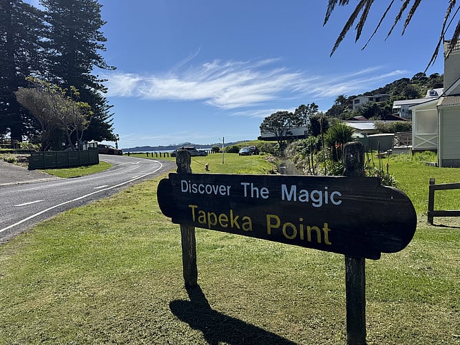 Dark rustic wooden welcome sign reading Discover The Magic Tapeka Point along the coastal road in Russell, Bay of Islands